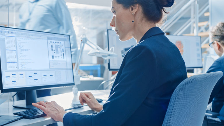 Nainen työskentelee sinisessä jakussa tietokoneella datan parissa.